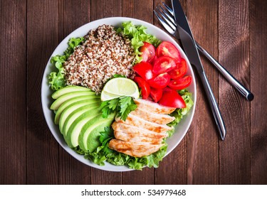 Healthy Salad Plate With Quinoa, Cherry Tomatoes, Chicken, Avocado, Lime And Mixed Greens, Lettuce, Parsley On Wooden Background Top View. Food And Health. Superfood Meal.