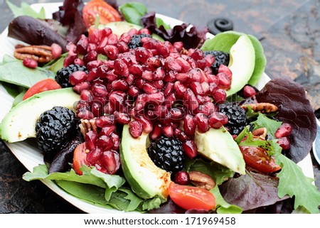 A healthy salad with pomegranate, avocado, tomatoes, almonds and argula lettuce over a rustic background. 