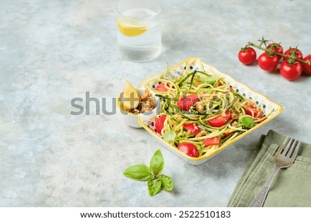 Healthy salad, zucchini spaghetti with cherry tomatoes and walnuts in a colorful plate on a gray concrete background. Vegan recipes. Zucchini recipes