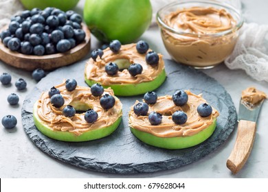Healthy sandwich. Green apple rounds with peanut butter and and blueberries on slate board, horizontal