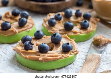 Healthy sandwich. Green apple rounds with peanut butter and and blueberries on wooden table, horizontal