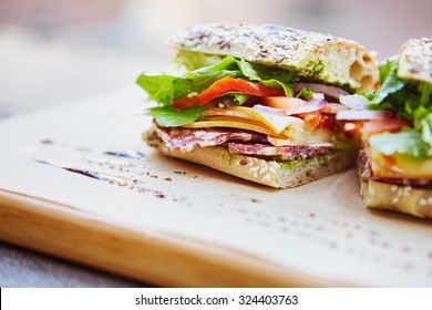 Healthy sandwich made of a fresh seeded roll, cut in half to display tasty ingredients of salami, tomato, lettuce and chess, presented on a wooden board