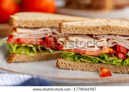 Healthy sandwich with turkey, tomato and lettuce on whole wheat bread on a white plate