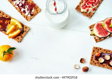 Healthy Sandwiches With Chocolate Paste, Soft Cheese, Fig, Orange, Cranberry Jam, Pomegranate On Crisp Rye Bread And Jug Of Milk On A White Table. Copy Space.