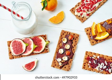 Healthy Sandwiches With Chocolate Paste, Soft Cheese, Fig, Orange, Cranberry Jam, Pomegranate On Crisp Rye Bread And Jug Of Milk On A White Table. 