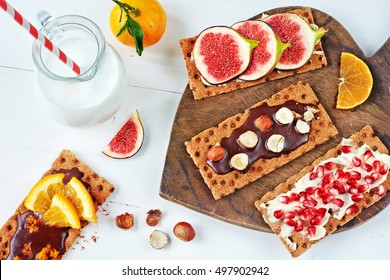 Healthy Sandwiches With Chocolate Paste, Soft Cheese, Fig, Orange, Cranberry Jam, Pomegranate On Crisp Rye Bread And Jug Of Milk On A White Table. 