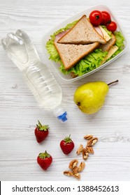 Healthy School Lunch Box With Fresh Organic Vegetables Sandwiches, Walnuts, Bottle Of Water And Fruits On A White Wooden Table, Overhead. From Above. Top View.