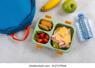 Healthy school lunch box with sandwich and salad on the workplace near backpack. School supplies, books, apple and a bottle of water. Back to school