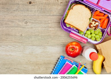 Healthy school lunch and school supplies. Overhead view side border on a wood background.