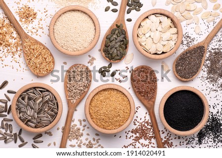 Healthy seeds - sesame, flax seed, sunflower seeds, pumpkin seed, chia and black seed in wooden spoons and bowls on a white background. Top view