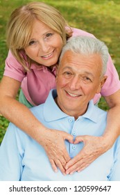 Healthy senior couple in park. Female showing heart symbol on his chests.