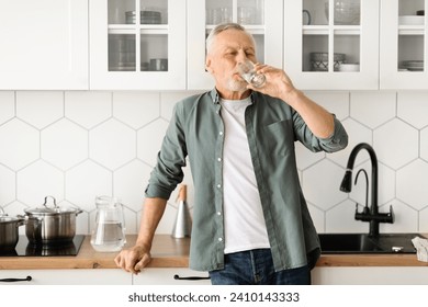 Healthy senior man drinking glass of water in his kitchen, elderly gentleman showcasing the importance of hydration for well-being, standing in relaxed posture, reflecting healthy lifestyle - Powered by Shutterstock