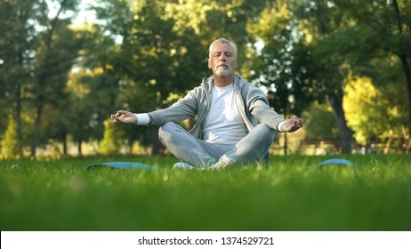 Healthy senior man meditating in park, sitting lotus pose on yoga mat, zen - Powered by Shutterstock