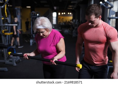 Healthy Senior Woman Exercising With Personal Trainer, Doing Bicep Curls With Bodybar