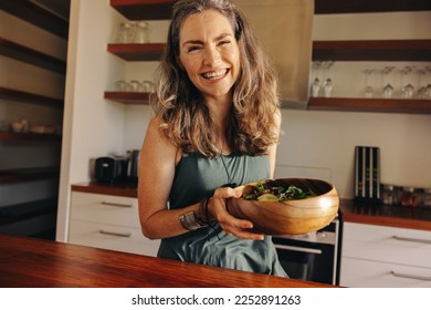 Healthy senior woman smiling happily while holding a wholesome buddha bowl. Mature woman serving herself a delicious vegan meal at home. Woman taking care of her aging body with a plant-based diet. - Powered by Shutterstock