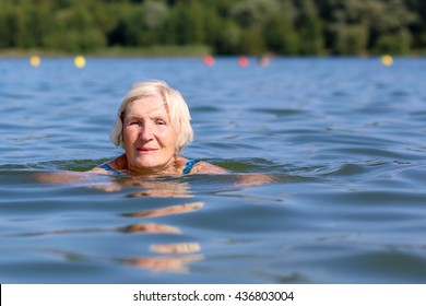 Healthy Senior Woman Swimming In The Lake Or River. Happy Elderly Lady Enjoying Active Summer Vacation. Sportive Lifestyle. Active Retirement Concept.