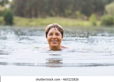 Healthy Senior Woman Swimming In The Lake Or River. Happy Elderly Lady Enjoying Active Summer Vacation. Sportive Lifestyle. Active Retirement Concept.