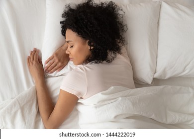Healthy serene young african american girl sleeping well in comfortable cozy fresh bed on soft pillow white linen orthopedic mattress, calm sleepy black woman enjoy peaceful sleep at home, top view