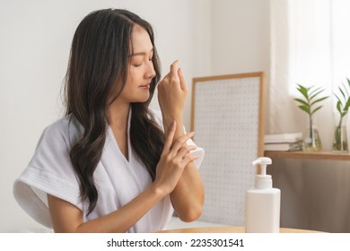Healthy skin care, beauty asian young woman in bathrobe, towel after shower bath at home, hand in applying, putting moisturizer on her arm. Skin body cream moisturizing lotion, routine in the morning