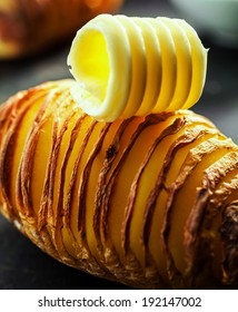 Healthy Sliced Baked Potato Cooked With The Jacket On In Foil And Served Topped With A Creamy Butter Curl On A Dark Background, Close Up View