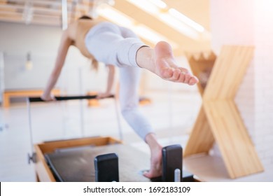 Healthy Smiling Brunette Woman Wearing Sportswear and Practicing Pilates in Exercise Studio On Reformer Special Equipment. Female doing reformer exercises on pilates machines indoors. Back view.