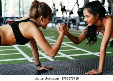 Healthy smiling female supportive friends giving high five to each other while pushing up in the fitness gym. Asian sporty people working out together. Teamwork and achievement concept