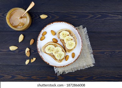 Healthy Snack From Bread With Almond Spread , Toast With Peanut Butter, Banana And Almond Nuts On Dark Wooden Background.  Flat Lay, Top View