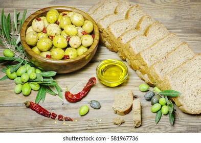 Healthy snack with fresh whole grain toast placed with pickles green and black olives, olive oil,raw olives and dry chili on rustic wooden table.Top view,copy space
