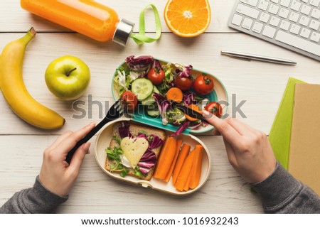 Healthy snack at office workplace. Businesswoman eating organic vegan meals from take away lunch box at wooden working table with computer keyboard