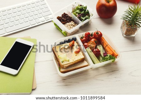 Healthy snack at office workplace. Organic vegetarian meals in take away lunch boxes at wooden working table with computer keyboard and smartphone