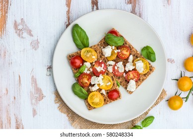 Healthy Snack from Wholegrain Rye Crispbread Crackers with Red and Yellow Cherry Tomatoes, Basil and Feta Cheese on the Light Background