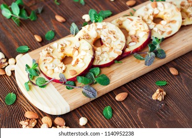 Gesunde Snacks - geschnittene Äpfel mit Honig und zerkleinerte Nüsse, mit Minze auf Holzbrett serviert