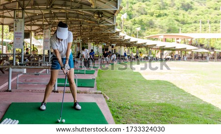 Healthy Sport.  Asian golfer woman swing golf ball practice at golf driving range on evening on time for healthy sport. Lifestyle and Sport Concept