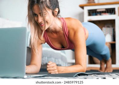 Healthy sport fitness lifestyle at home using laptop to watch and follow online lessons. Cheerful woman on the floor doing push ups plank exercise to build a perfect healthy body alone. Workout people - Powered by Shutterstock