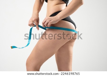 Healthy, sport and fitness lifestyles concept. Young woman in black underwear is measuring her thigh with measuring tape on white background.