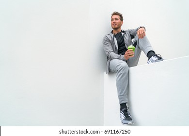 Healthy sport man drinking green smoothie during training at gym in activewear sweatpants outdoor. Athlete sitting relaxing post-workout.