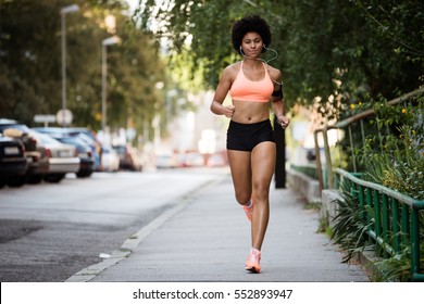 Sportswoman saudável correndo na calçada enquanto ouve música.