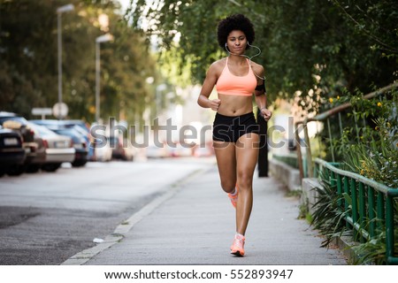 Healthy sportswoman running on sidewalk while listening to music.