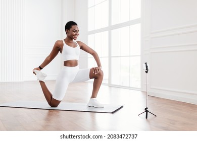 Healthy Sporty Lifestyle. Happy Black Fit Lady Stretching Back Leg Muscles And Quads Holding Feet Watching Online Tutorial Or Recording Fitness Video For Her Sport Blog, Using Cell Phone On Tripod