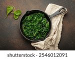 Healthy steamed spinach in cast iron pan on brown rustic background top view