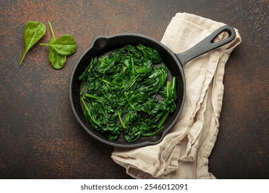 Healthy steamed spinach in cast iron pan on brown rustic background top view