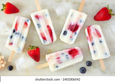 Healthy strawberry blueberry summer yogurt popsicles, top view scattered on a white marble background