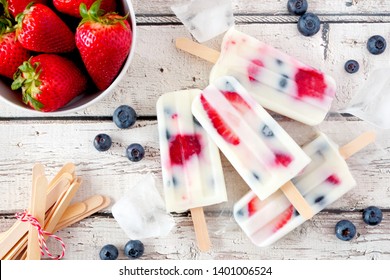 Healthy strawberry blueberry yogurt popsicles, top view summer table scene against a white wood background