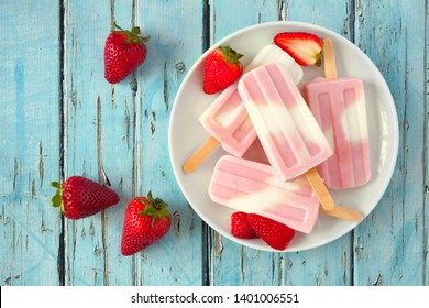 Healthy strawberry yogurt summer popsicles on a plate, top view table scene against a blue wood background