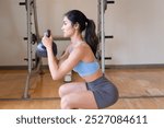 Healthy strong Asian fitness woman working out in indoors gym, kettlebell goblet squat for glutes, quadriceps, hamstrings, glutes, forearms, shoulder, core, lower back muscle weight bearing training