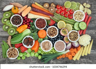 Healthy super food sampler with fresh vegetables, fruit and herbal medicine, in porcelain dishes and loose, top view on rustic background. Health food concept high in antioxidants & anthocyanins.