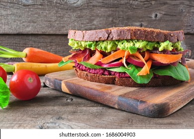 Healthy Superfood Sandwich With Avocado, Beet Hummus, Spinach Radishes And Carrots. Side View Table Scene Against A Dark Wood Background.