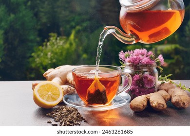 Healthy tea poured into transparent cup. Teapot, lemon, ginger, cardamom, heather bunch and glass jar of daisy teabags and water droplet splash.  - Powered by Shutterstock