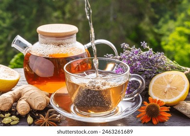 Healthy tea poured into transparent cup. Teapot, lemon, ginger, cardamom, heather bunch and glass jar of daisy teabags and water droplet splash.  - Powered by Shutterstock