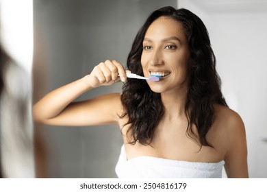 Healthy teeth and morning routine care. Woman brushing teeth with toothbrush and looking in mirror in bathroom - Powered by Shutterstock